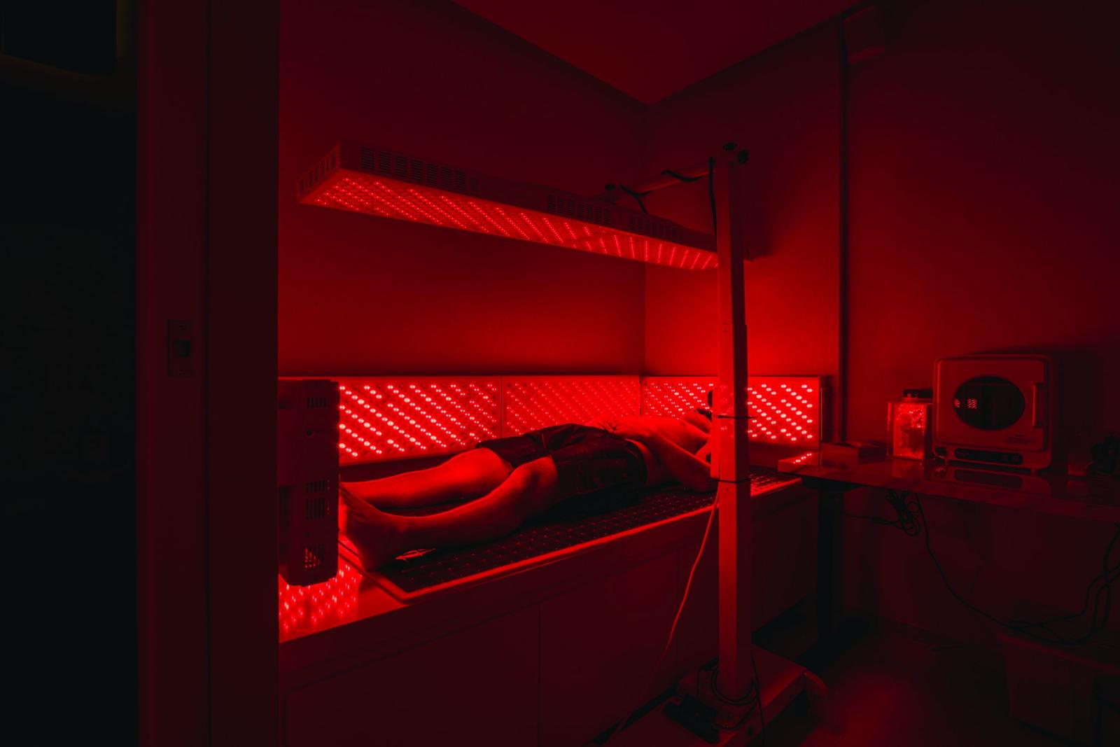 A client lying beneath full-body red LED panels in the darkened photobiomodulation room at The Longevity Science Centrum.