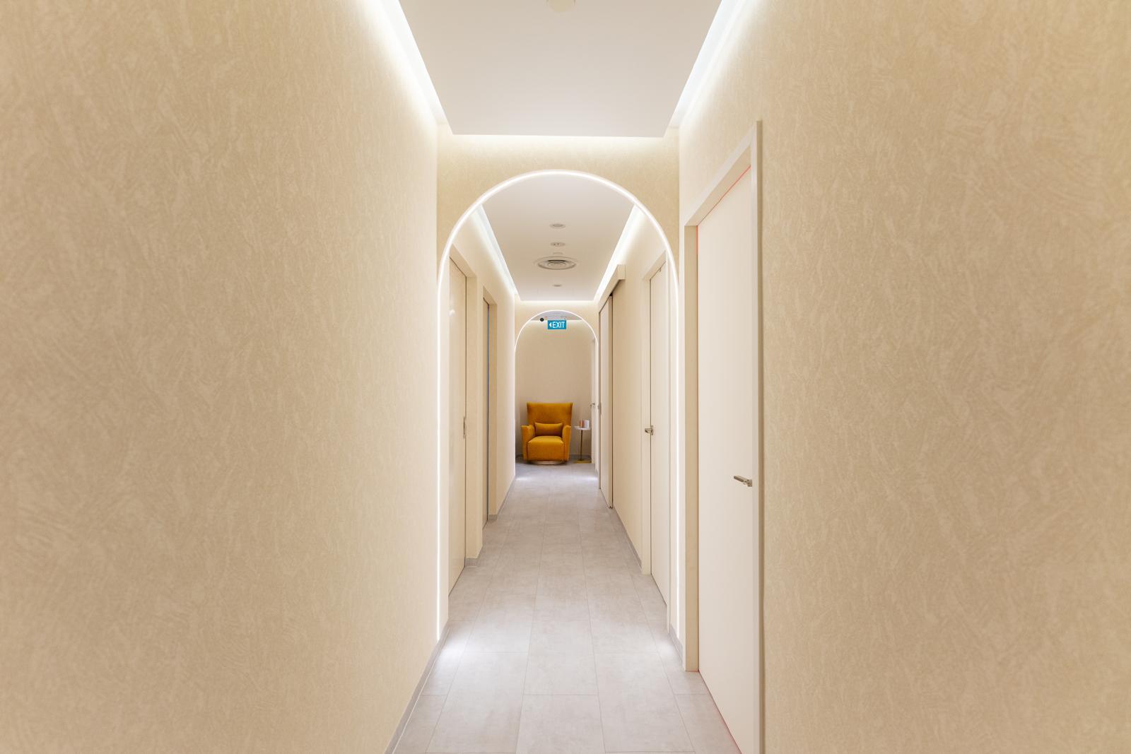 The arched, softly lit corridor at The Longevity Science Centrum leading past treatment room doors to a mustard armchair.